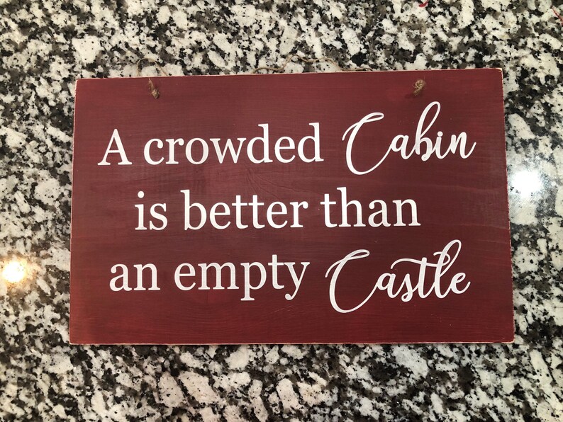 May include: A red wooden sign with white text that reads "A crowded Cabin is better than an empty Castle".