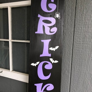 May include: Purple "TRICK" sign with white bats and a spider on a black background.