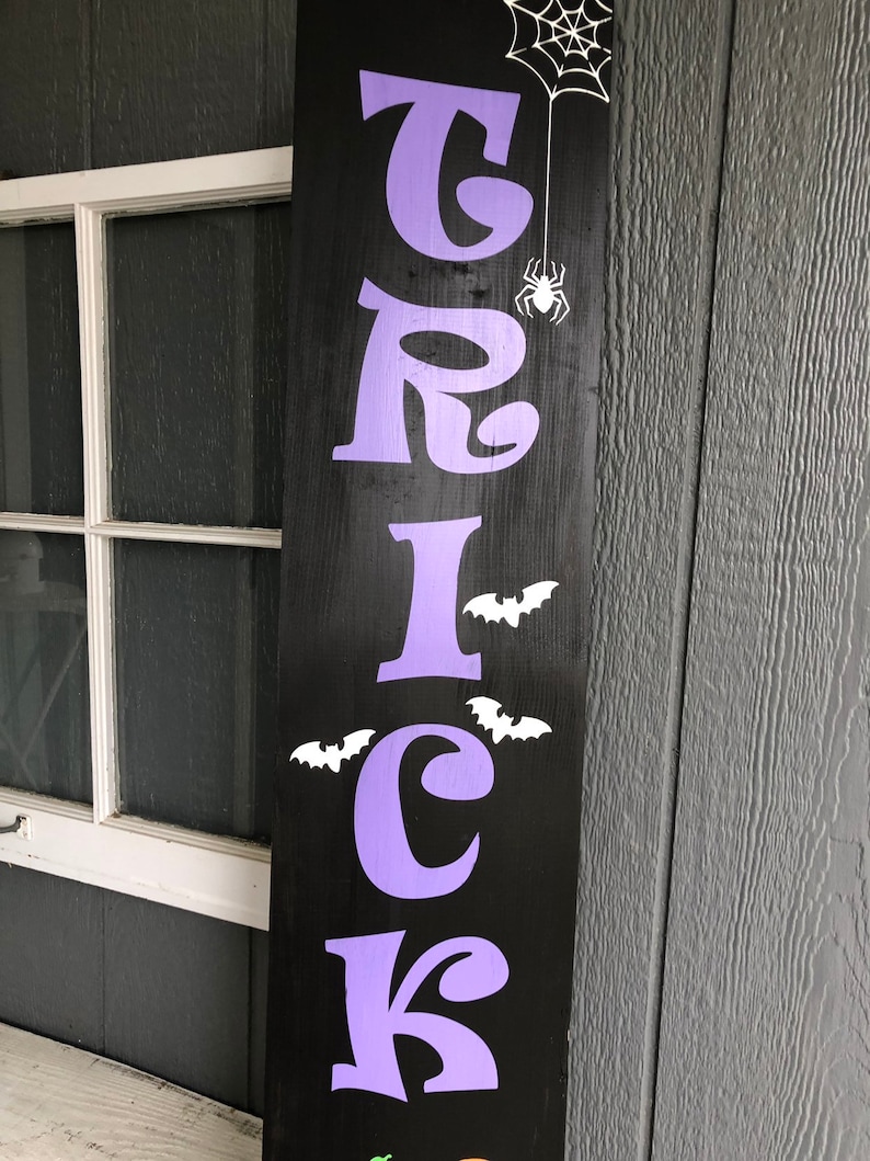 May include: Purple "TRICK" sign with white bats and a spider on a black background.