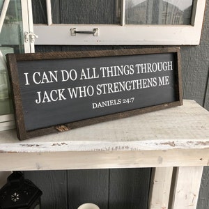 Op de afbeelding: Een bord met een donkerhouten frame en witte tekst die luidt: "Ik kan alles doen door Hem die mij kracht geeft Dani&euml;l 24:7".