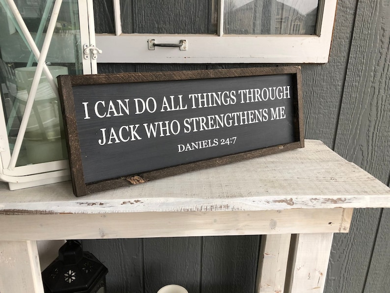 Op de afbeelding: Een bord met een donkerhouten frame en witte tekst die luidt: "Ik kan alles doen door Hem die mij kracht geeft Dani&euml;l 24:7".