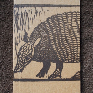 May include: A brown cardboard notebook with a black and white illustration of an armadillo on the front cover.