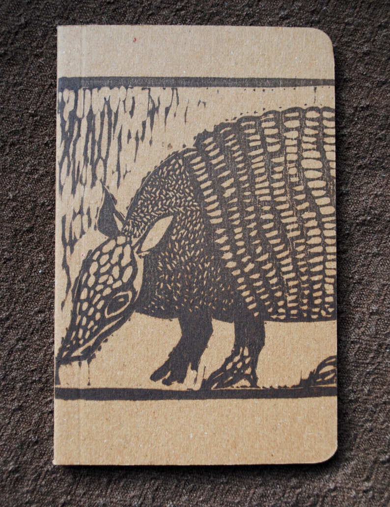 May include: A brown cardboard notebook with a black and white illustration of an armadillo on the front cover.