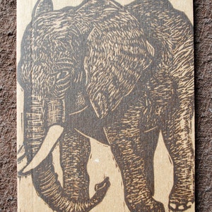 May include: A black and white linocut print of an elephant walking. The print is on a brown paper background.