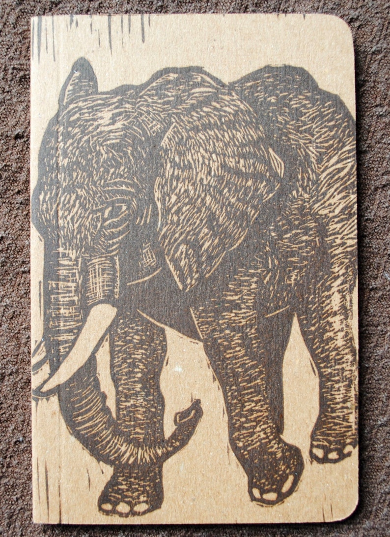 May include: A black and white linocut print of an elephant walking. The print is on a brown paper background.