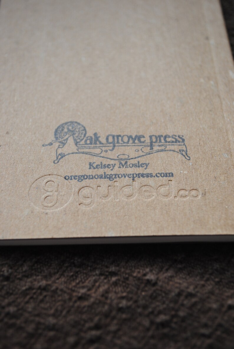 May include: A brown paper book with a black and white illustration of a snail on the back cover. The text "Oak Grove Press" is printed above the snail illustration. The text "Kelsey Mosley" is printed below the snail illustration. The text "oregon@oakgrovepress.com" is printed below the name. The text "guided.co" is printed below the email address.