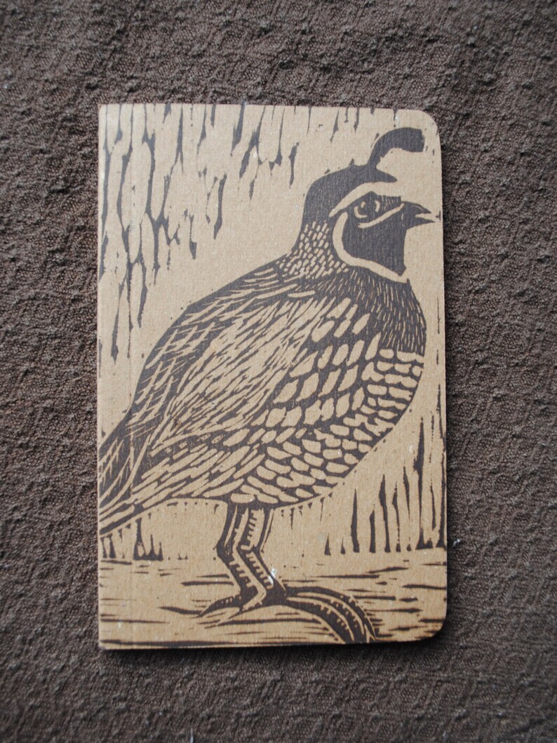 May include: A brown and black linocut print of a quail on a brown background. The quail is facing right and has a detailed pattern of feathers.