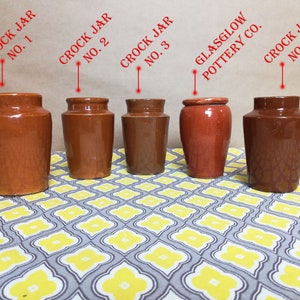 Puede incluir: Cuatro tarros de cerámica marrón con el texto "Crock Jar" y un número del 1 al 4 en cada tarro. Los tarros están dispuestos en una fila sobre una superficie con estampado gris y amarillo. El tarro del medio tiene el texto "Glasglow Pottery Co."