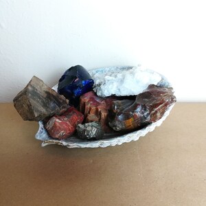 May include: A collection of colorful crystals and stones, including blue, red, brown, and white, displayed in a white ceramic bowl.