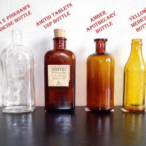 May include: Four glass bottles of different colors and shapes. The bottles are labeled with the text "Lydia E Pinkham's Medicine Bottle", "Amitriptyline Hydrochloride Tablets USP Bottle", "Amber Apothecary Bottle", and "Yellow Medicine Bottle".