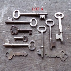 May include: A collection of ten antique keys, some with intricate designs, including a key with a flower-shaped head, a key with a double-loop head, and a key with a single-loop head. The keys are arranged on a gray surface with the text "LOT A" written in red.
