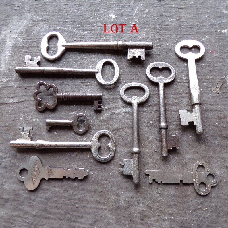 May include: A collection of ten antique keys, some with intricate designs, including a key with a flower-shaped head, a key with a double-loop head, and a key with a single-loop head. The keys are arranged on a gray surface with the text "LOT A" written in red.