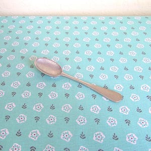 May include: A silver-toned metal spoon featuring a textured, hammered finish on both the bowl and the handle. The spoon has an oval-shaped bowl and a slender, slightly tapered handle, presenting a uniform metallic appearance throughout the piece.