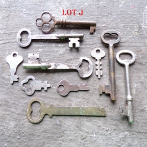 May include: A collection of ten antique keys, some with ornate designs, including a key with the words "GOODWILL CONN USA" on it. The keys are arranged on a gray surface with the text "LOT J" in red letters at the top of the image.