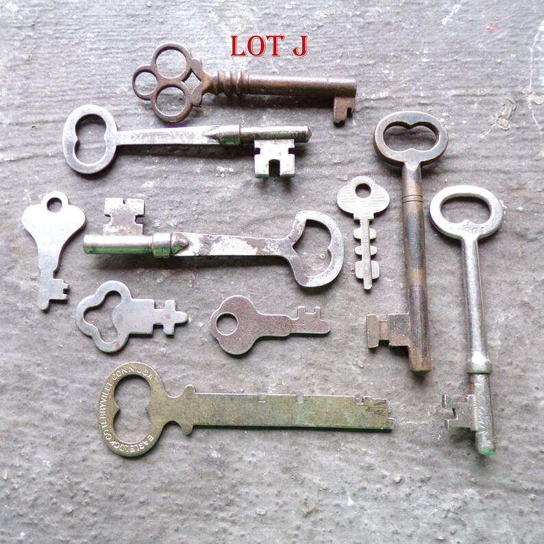 May include: A collection of ten antique keys, some with ornate designs, including a key with the words "GOODWILL CONN USA" on it. The keys are arranged on a gray surface with the text "LOT J" in red letters at the top of the image.