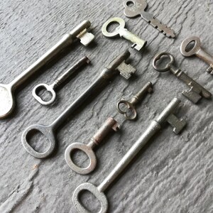 May include: A collection of vintage keys in various sizes and styles, including skeleton keys, ward keys, and a key with a decorative handle. The keys are made of metal and have a silver finish.