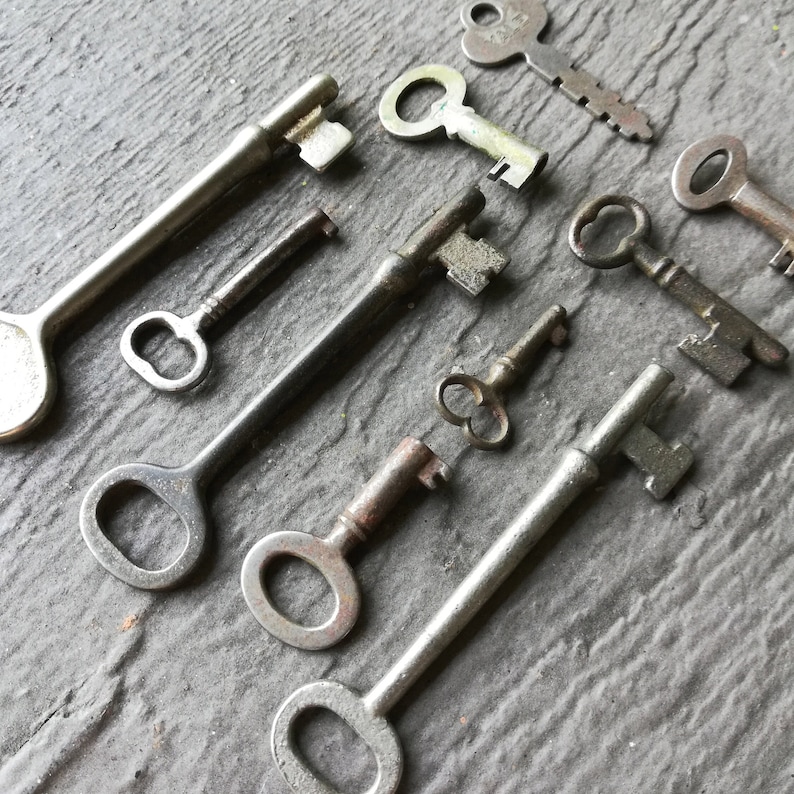 May include: A collection of vintage keys in various sizes and styles, including skeleton keys, ward keys, and a key with a decorative handle. The keys are made of metal and have a silver finish.
