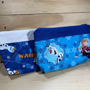 May include: Two blue and white zippered pouches with a Frozen theme. One pouch features Olaf and the text "I  WARM", the other pouch features Elsa and Olaf.