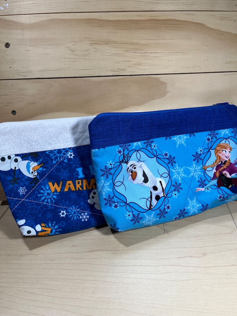 May include: Two blue and white zippered pouches with a Frozen theme. One pouch features Olaf and the text "I  WARM", the other pouch features Elsa and Olaf.