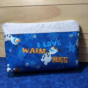 May include: Blue quilted zippered pouch with a white border. The pouch features a snowman design with the text "I love warm hugs".