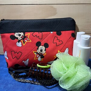 Puede incluir: Bolsa roja acolchada con cremallera con estampado de Mickey Mouse. La bolsa est&aacute; llena de una esponja de ba&ntilde;o verde, una pinza para el pelo marr&oacute;n y dos botellas transparentes etiquetadas como "cleanse".