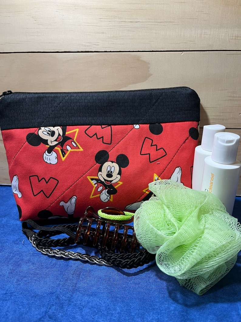 Puede incluir: Bolsa roja acolchada con cremallera con estampado de Mickey Mouse. La bolsa est&aacute; llena de una esponja de ba&ntilde;o verde, una pinza para el pelo marr&oacute;n y dos botellas transparentes etiquetadas como "cleanse".
