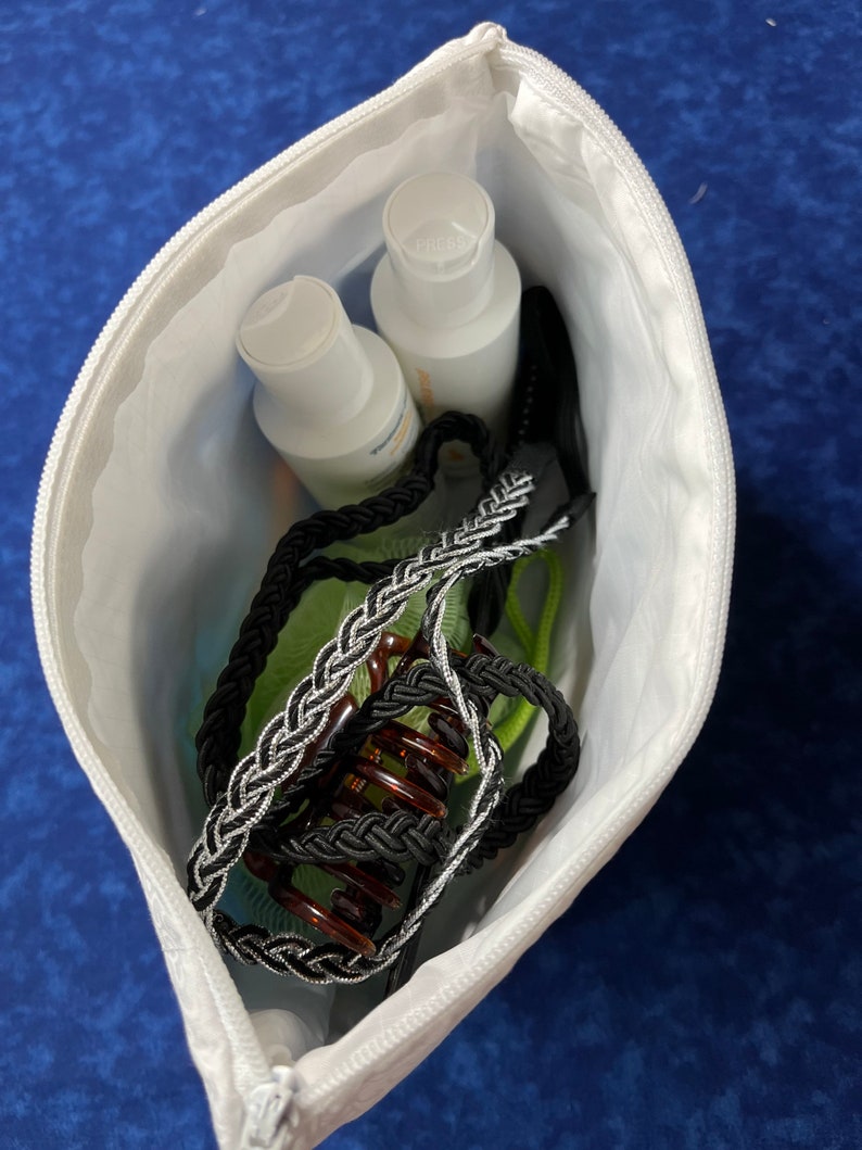 May include: A white zippered pouch containing two clear bottles of lotion, a black and silver braided hair tie, and a brown hair clip.