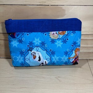 May include: A blue zippered pouch with a quilted design. The pouch features a snowflake pattern and images of characters from the film Frozen, including Olaf, Elsa, and Anna.