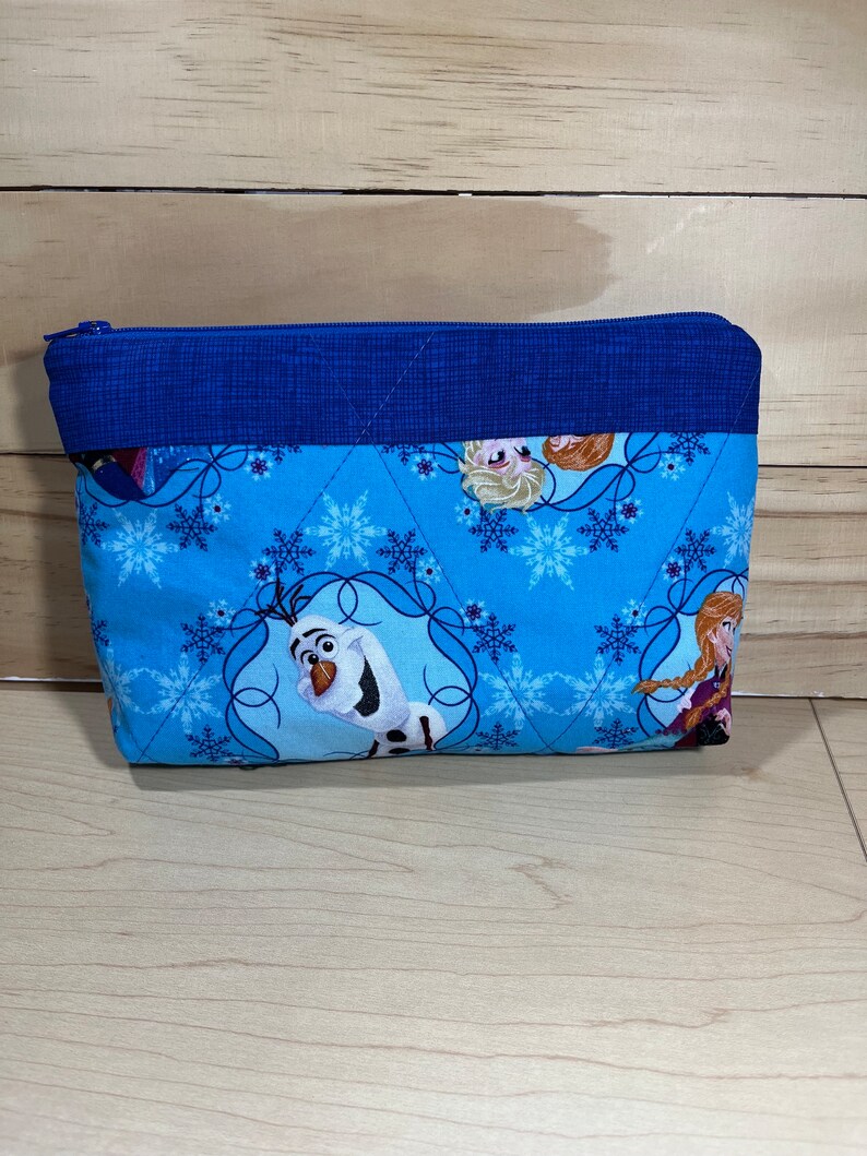 May include: A blue zippered pouch with a quilted design. The pouch features a snowflake pattern and images of characters from the film Frozen, including Olaf, Elsa, and Anna.