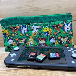 May include: A gray Nintendo Switch Lite console with three game cartridges and a green zippered pouch. The pouch features a colorful pattern of Animal Crossing characters on a green background.