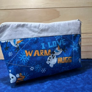 May include: Blue quilted zippered pouch with a white trim. The pouch features a snowman design and the text "I love warm hugs".