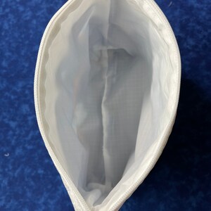 May include: White zippered pouch with a white lining. The pouch is open and the zipper is visible.