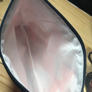 Puede incluir: Una bolsa negra con cremallera y forro rosa. La bolsa est&aacute; hecha de una tela con un patr&oacute;n geom&eacute;trico.