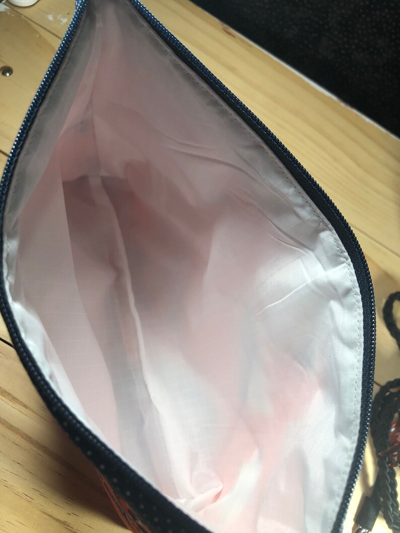 Puede incluir: Una bolsa negra con cremallera y forro rosa. La bolsa est&aacute; hecha de una tela con un patr&oacute;n geom&eacute;trico.