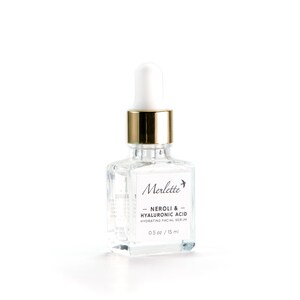 May include: A clear glass bottle of Merlette Neroli & Hyaluronic Acid Hydrating Facial Serum. The bottle has a white dropper top with a gold collar and a white label with black text. The bottle contains 0.5 oz / 15 ml of serum.
