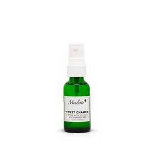 Peut inclure: Une bouteille en verre vert avec un vaporisateur blanc. La bouteille porte une &eacute;tiquette blanche avec le texte "Merlette SWEET CHAMPA SERUM WITH VITAMIN C & HYALURONIC ACID 30 ml". Sur fond blanc.