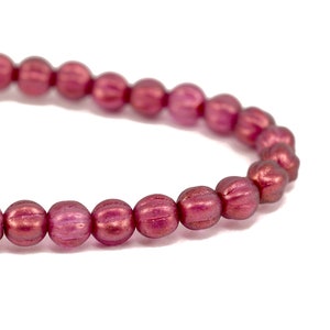 May include: A strand of small, round, red beads with a metallic sheen. The beads have a slightly textured surface.