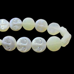 May include: A strand of pale yellow and white beads. The beads are round with a carved design. The beads are strung together on a string. The background is black.