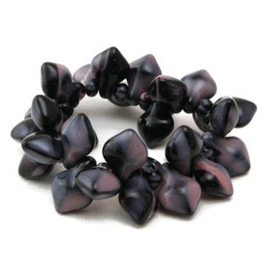 May include: A strand of dark purple and pink glass beads with a faceted, irregular shape. The beads are arranged in a circle, creating a bracelet or necklace.