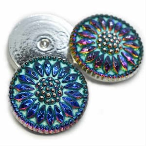 May include: Two iridescent blue and green glass buttons with a silver metal backing. The buttons feature a floral design with a raised centre.