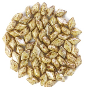 May include: A pile of small, light brown, diamond-shaped glass beads with a speckled pattern.