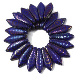 May include: A collection of deep blue, teardrop-shaped beads arranged in a circular pattern. Each bead features a metallic, iridescent design with swirling and linear patterns. The beads are likely for jewelry making.