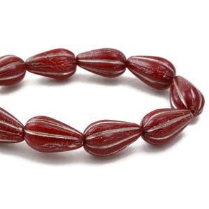 May include: A strand of red glass beads with white stripes. The beads are shaped like teardrops.