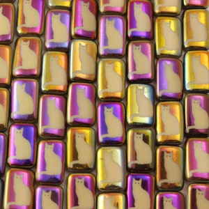 May include: A collection of iridescent glass tiles with a white cat silhouette design. The tiles are rectangular and have a variety of colors, including purple, pink, gold, and green.