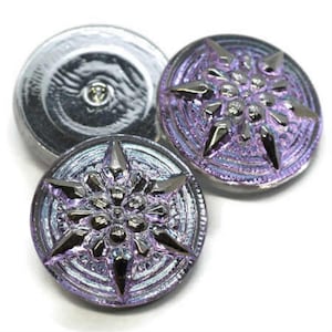 May include: Two iridescent purple glass buttons with a silver snowflake design. The buttons have a raised, textured surface.