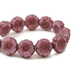 May include: A strand of pink glass beads with a flower design. The beads have a metallic sheen and are strung together to form a bracelet.