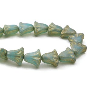 May include: A strand of turquoise-colored, bell-shaped beads with gold accents. The beads are arranged in a curved line, showcasing their unique floral design and textured surface. These beads are ideal for jewelry making.