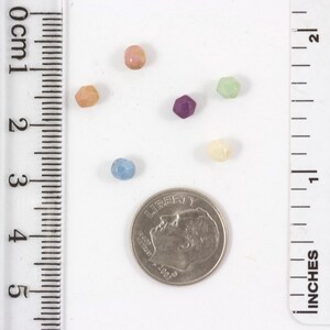 May include: Assortment of six small glass beads in various colors, including pink, purple, blue, green, and cream. The beads are displayed next to a US dime for size comparison.