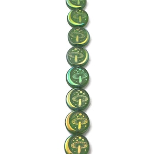 May include: Green, iridescent glass beads with a mushroom and crescent moon design. The beads are round and have a flat back. The mushroom and moon are in a lighter shade of green and yellow.