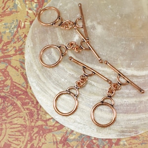 May include: Three copper toggle clasps with round rings. The clasps are made of metal and have a polished finish.